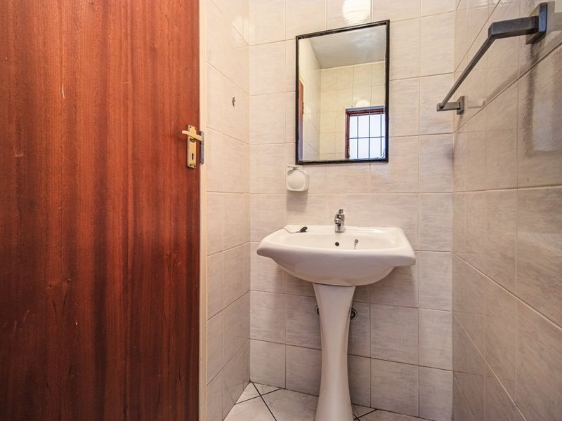 A compact bathroom featuring a pedestal basin, wall-mounted mirror, and neutral ceramic tiling throughout.