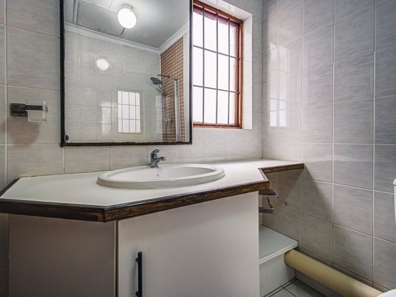 A dated bathroom featuring a vanity cabinet with a drop-in sink, tiled walls, and a shower enclosure, requiring cosmetic updates to modernize the space.