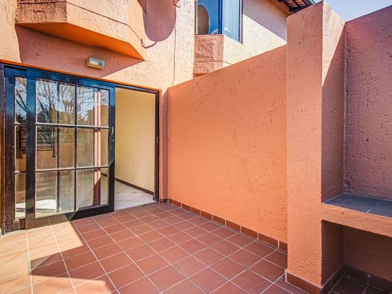 A private outdoor patio area featuring tiled flooring, a built-in braai, and direct access to the interior through a sliding glass door.