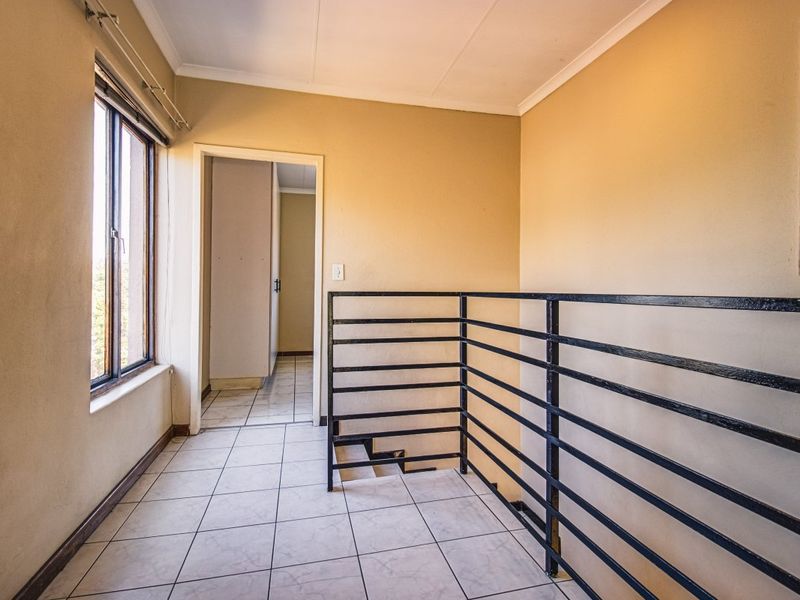 A vacant upper-level hallway featuring tiled flooring and a black metal safety railing overlooking the staircase.