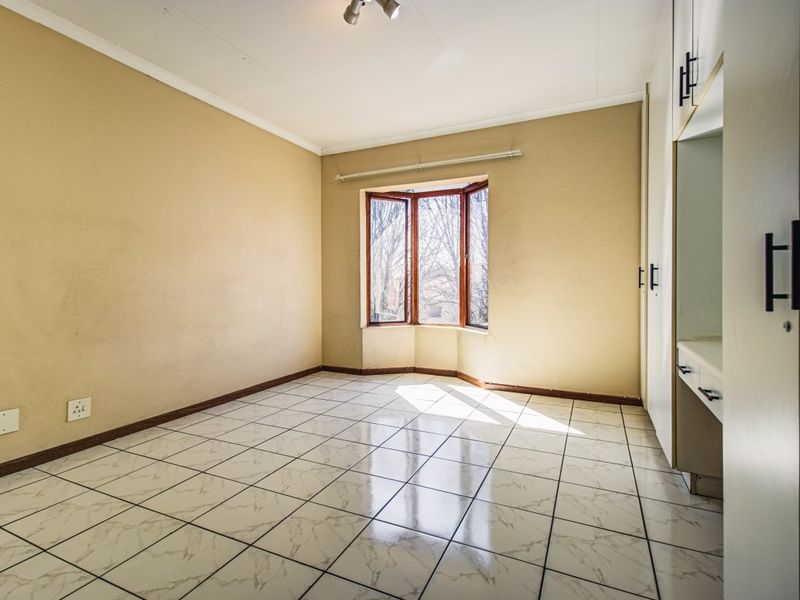 An empty bedroom featuring tiled flooring, built-in cupboards with a vanity area, and a bay window allowing natural light.