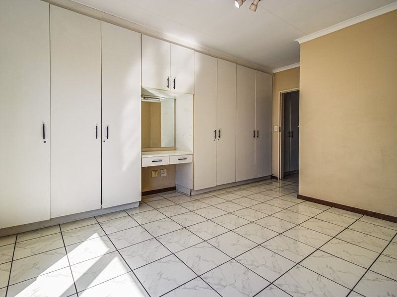A spacious bedroom featuring extensive built-in cupboards with an integrated vanity station and clean, light-toned tiled flooring throughout.
