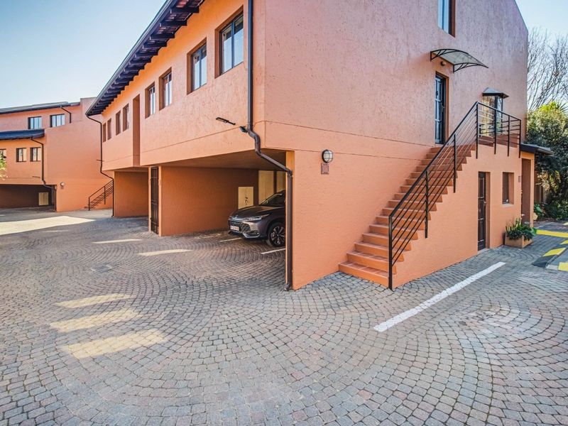 Exterior view of an apartment complex featuring a cobblestone driveway, covered parking bays, and an external staircase leading to upper-level units.