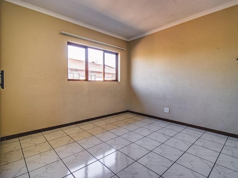 An empty bedroom featuring tiled flooring, neutral wall finishes, and a window, providing a blank canvas for personalization.
