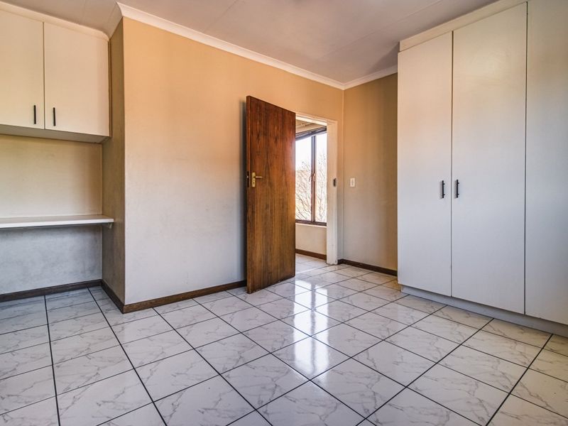 An empty bedroom featuring white tiled flooring, built-in cupboards, and a built-in desk area with neutral wall tones.