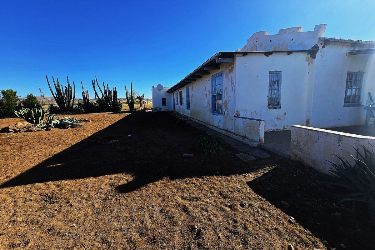 Rear elevation of a rustic property featuring white plastered walls, traditional casement windows, and a surrounding arid landscape.