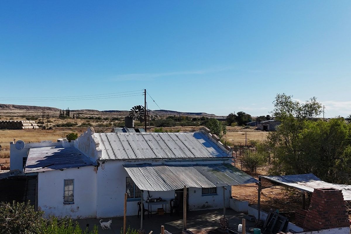 Aerial view of a rural property featuring a corrugated iron roof, covered patio, and traditional wind pump in a dry landscape setting.