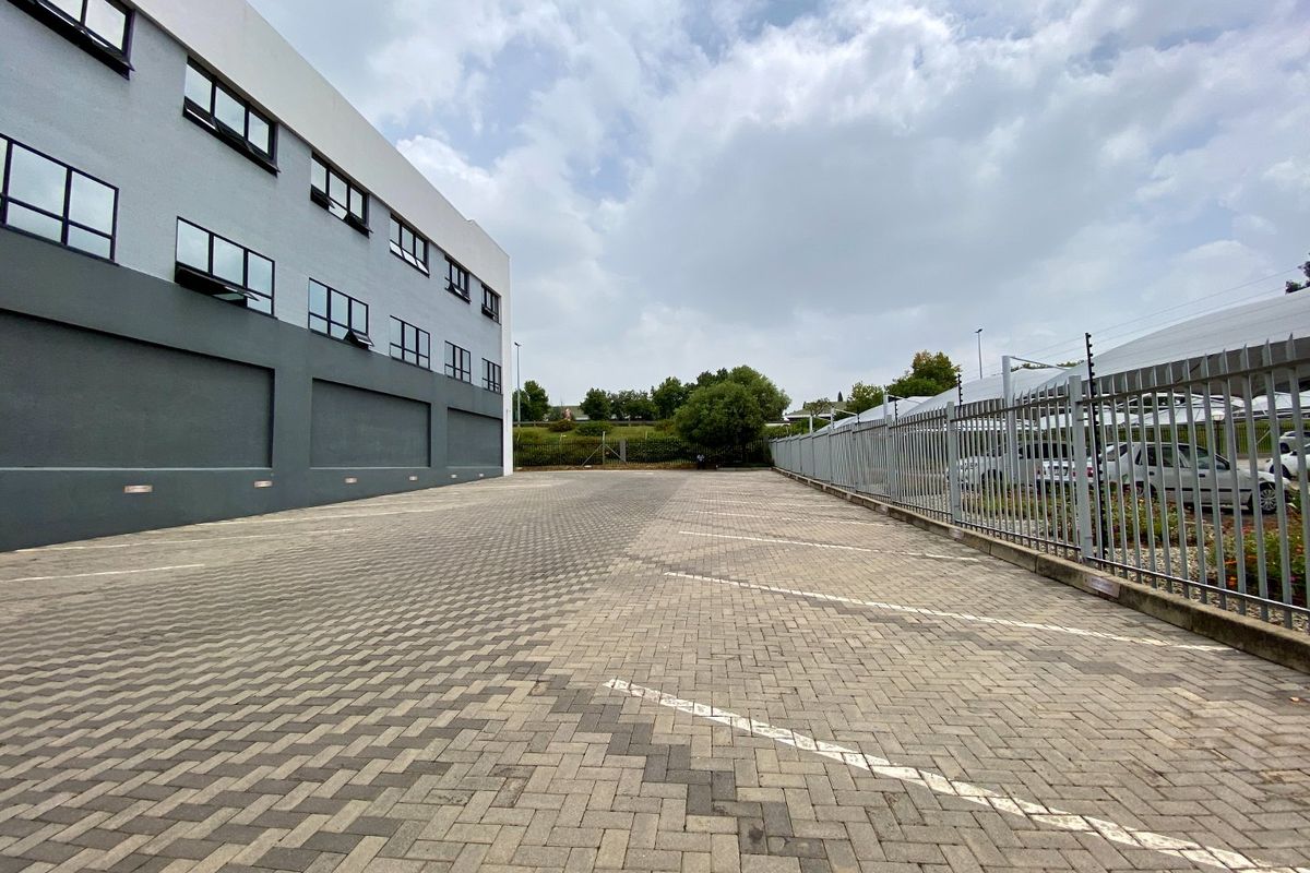 Spacious paved commercial parking area adjacent to a modern multi-story building, secured with perimeter fencing and electric security wires.