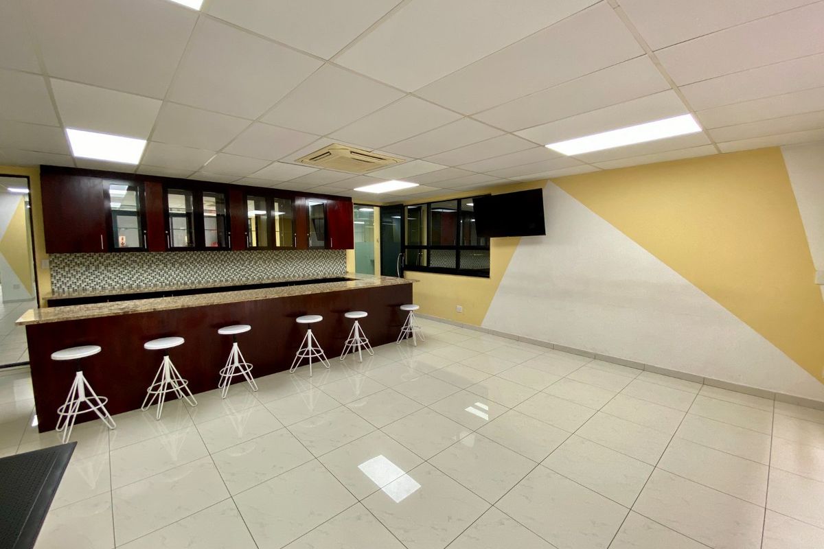 A commercial kitchen area featuring dark wood cabinetry, granite countertops, mosaic backsplash, and bright ceramic floor tiles with integrated ceiling lighting.