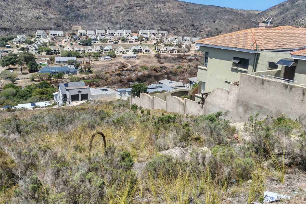 Elevated view overlooking a residential estate and surrounding hillside landscape from a vacant sloped plot.
