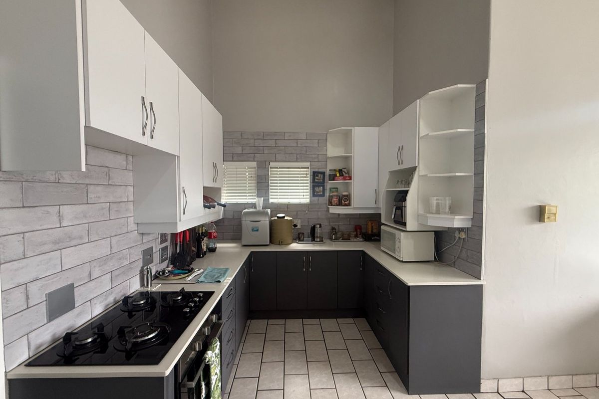 A modern U-shaped kitchen featuring dark lower cabinetry, white upper cabinets, a gas hob, built-in oven, and a stylish tiled backsplash.