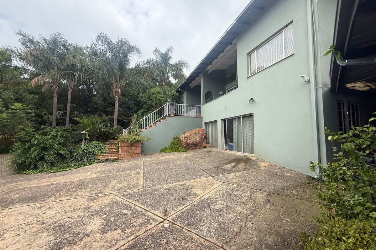 Rear exterior view of the property featuring a concrete driveway, external staircase with metal railing, and sliding glass doors leading to the lower level.