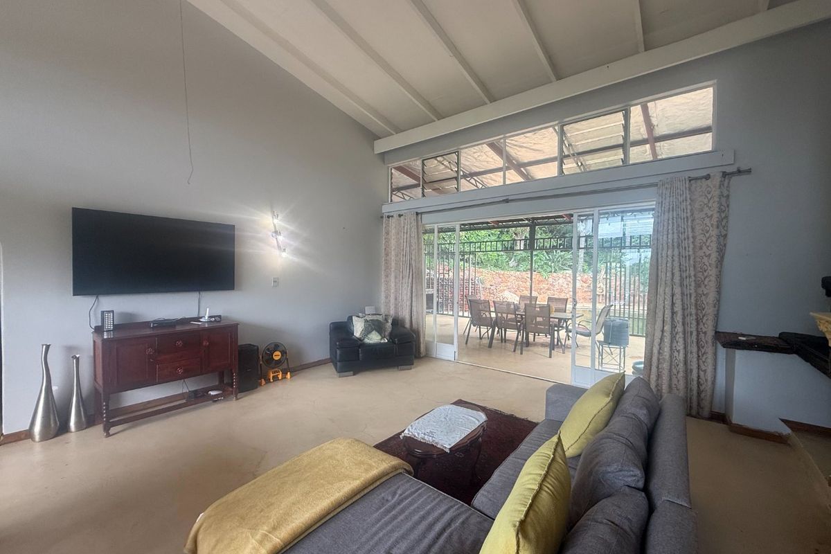Spacious living room featuring a high vaulted ceiling with exposed beams, concrete flooring, and large sliding glass doors opening to an outdoor patio area.