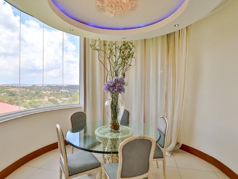 A bright dining area featuring a circular recessed ceiling with ambient lighting, large floor-to-ceiling windows, and panoramic views.