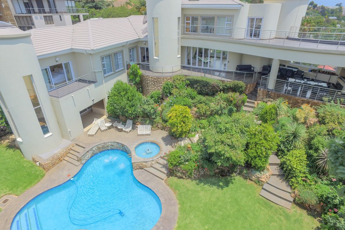 Aerial view of a luxury residence featuring a landscaped garden, swimming pool with spa, stone retaining walls, and multiple balconies.