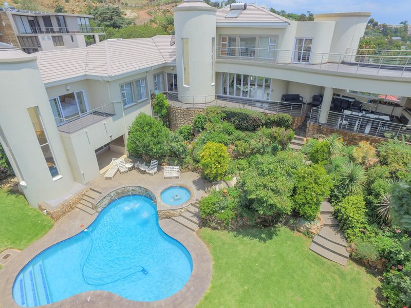 Aerial view of a luxury residence featuring a landscaped garden, swimming pool with spa, stone retaining walls, and multiple balconies.
