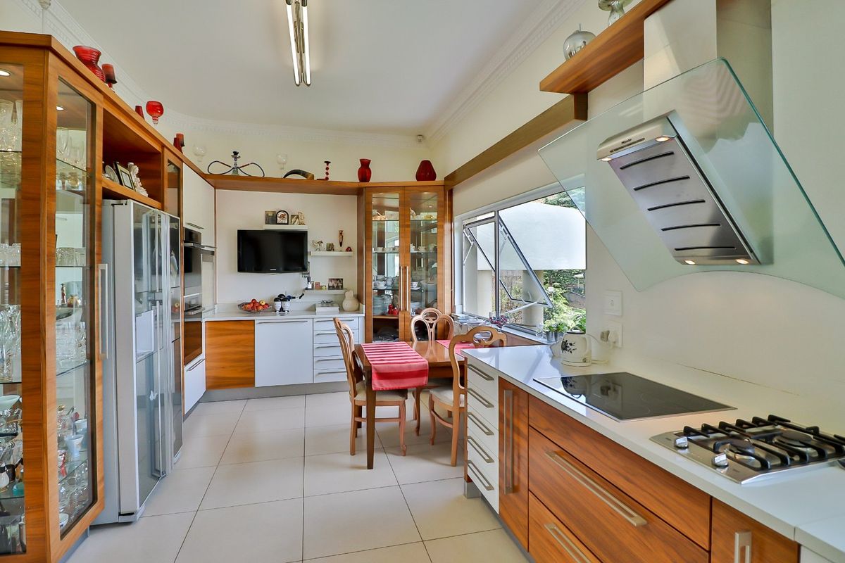 A well-maintained kitchen featuring wood-finish cabinetry, stone countertops, integrated appliances, and a dedicated dining area with large windows overlooking the garden.