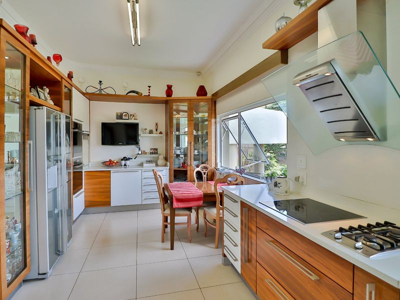 A well-maintained kitchen featuring wood-finish cabinetry, stone countertops, integrated appliances, and a dedicated dining area with large windows overlooking the garden.