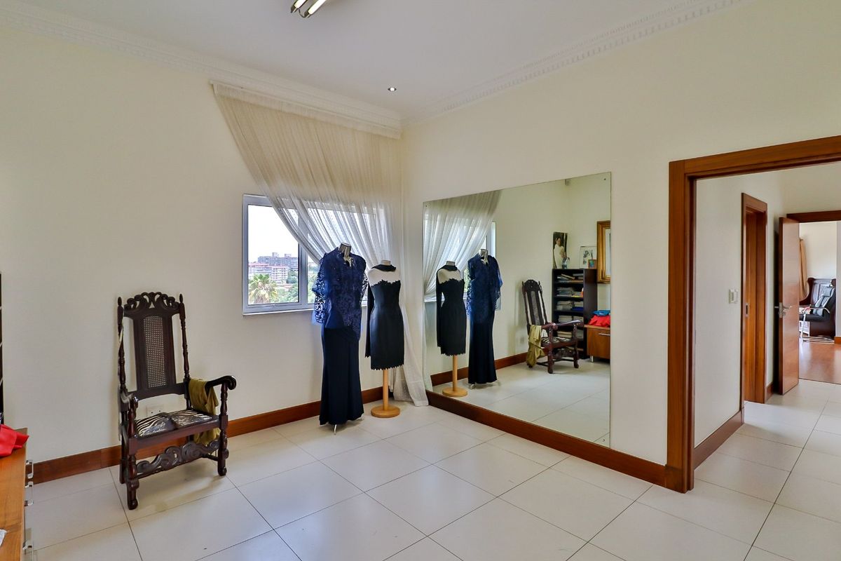 A spacious bedroom featuring large wall-mounted mirrors, neutral tiled flooring, and classic cornice detailing, offering a bright and versatile living space.