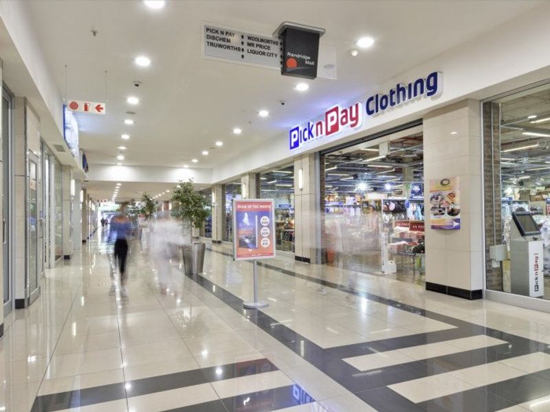 A well-maintained commercial shopping centre corridor featuring polished tiled flooring, recessed lighting, and clear glass storefronts for retail units.