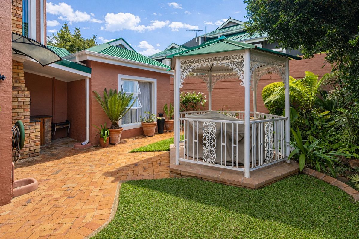 A private rear courtyard featuring brick paving, a landscaped garden, and a decorative metal gazebo, complemented by a built-in brick braai area.