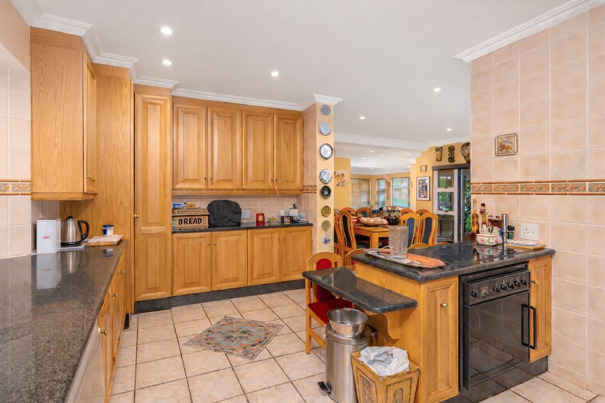A functional kitchen featuring oak cabinetry, granite countertops, built-in oven, and tiled flooring, with an open-plan layout connecting to the dining area.