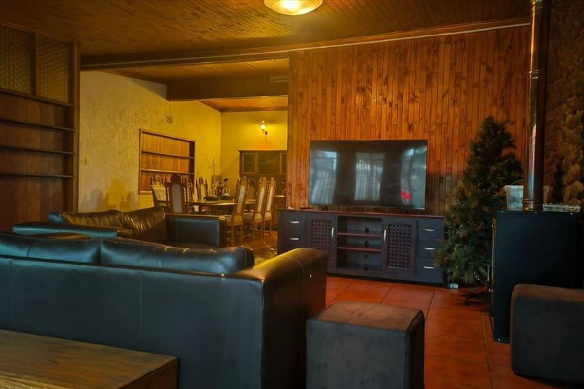 Spacious open-plan living and dining area featuring timber wall paneling, a stone feature wall, terracotta flooring, and a built-in fireplace.