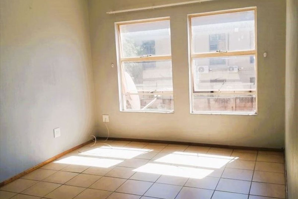 An empty bedroom featuring tiled flooring, neutral wall paint, and natural light from two windows with an installed curtain track.