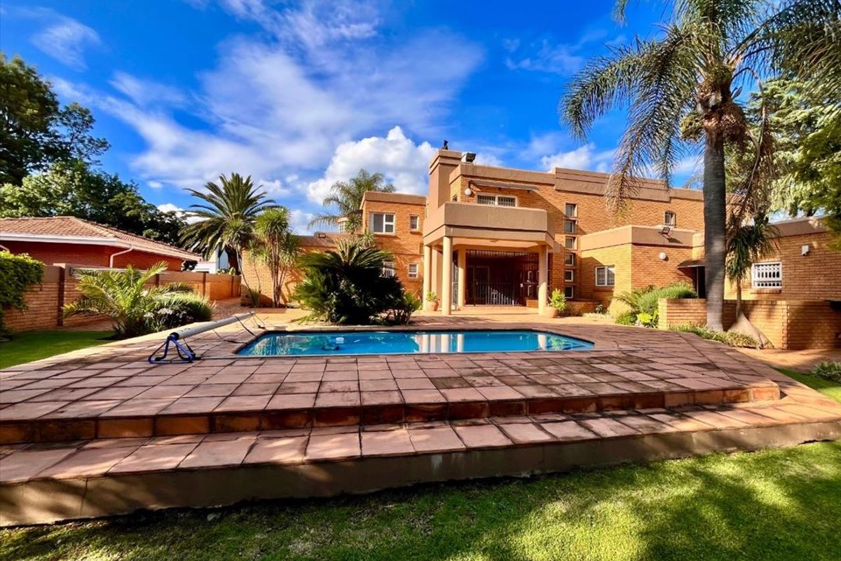 Rear view of the property featuring a brick facade, a raised tiled pool deck, and a well-maintained garden area.