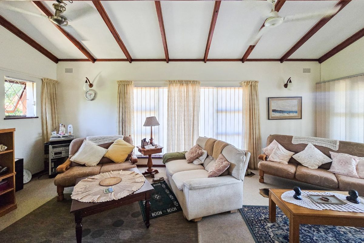 Spacious living room featuring exposed timber ceiling beams, ceiling fans, and large windows allowing for natural light.