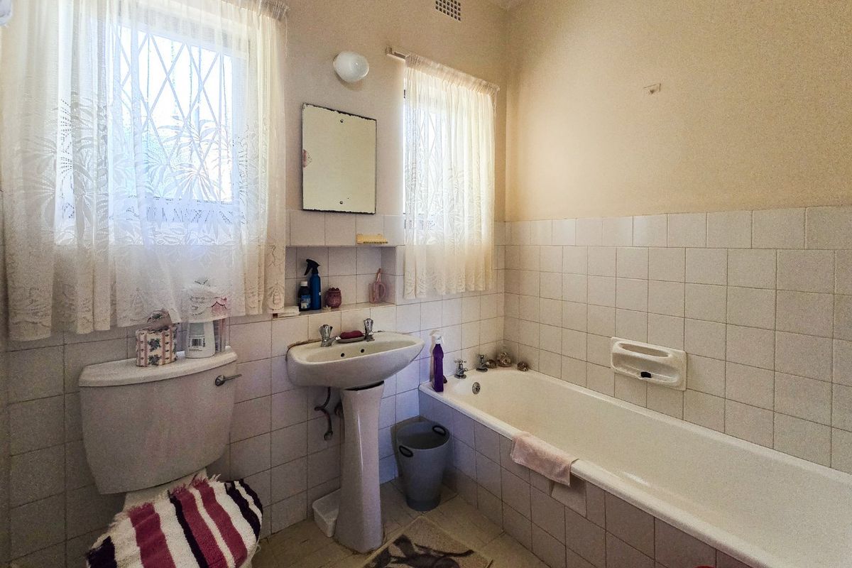 A dated bathroom featuring a pedestal washbasin, built-in bathtub, and ceramic tiling throughout, offering potential for a modern renovation.