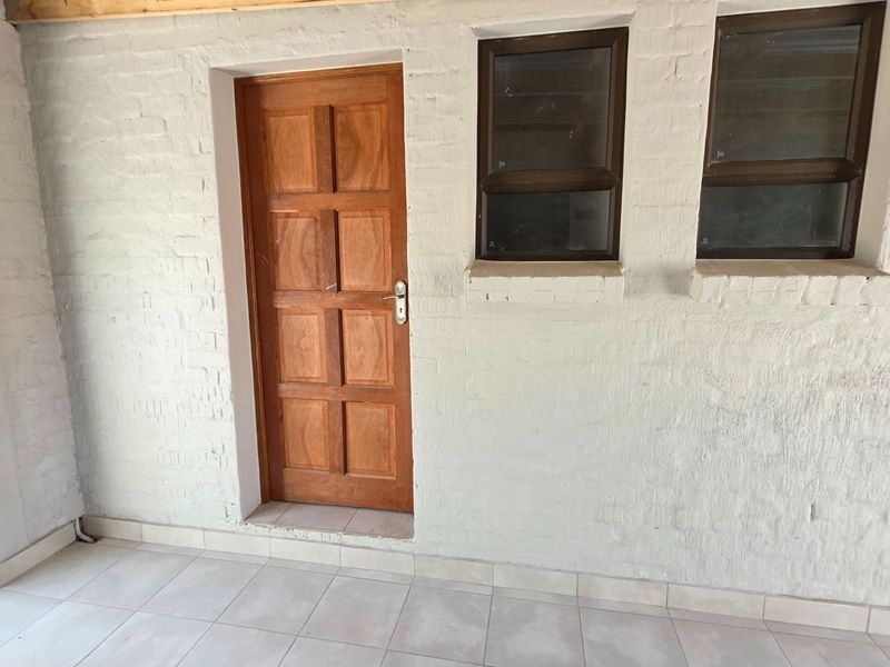 A covered patio area featuring tiled flooring, painted brick walls, and timber panel doors with aluminium frame windows.