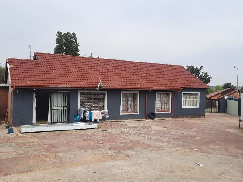 Rear view of a townhouse featuring a tiled roof, security gates, burglar bars, and a large paved courtyard area.