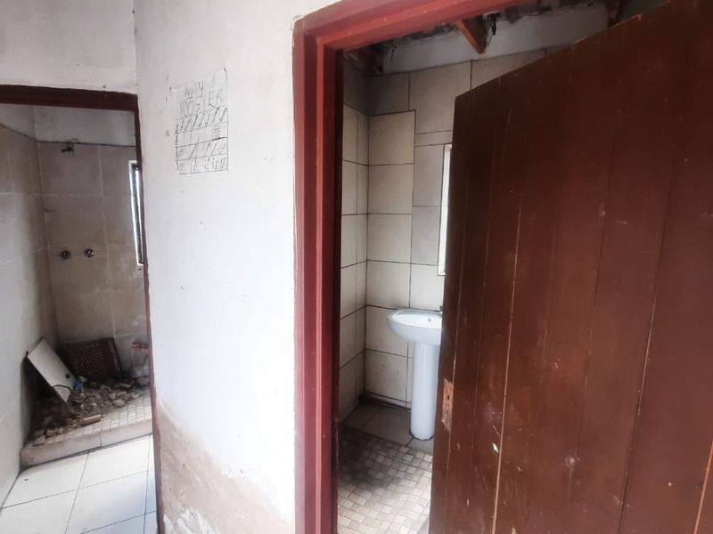 A bathroom area in need of significant renovation, featuring a pedestal basin, tiled surfaces, and visible structural damage to the walls and ceiling.