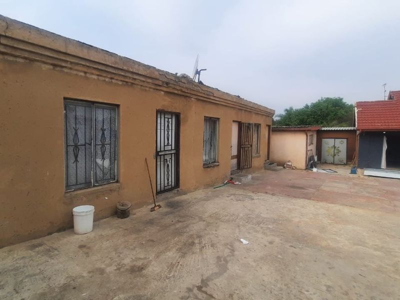 Rear exterior view of the townhouse featuring a concrete paved courtyard, security gates, and weathered exterior wall finishes.