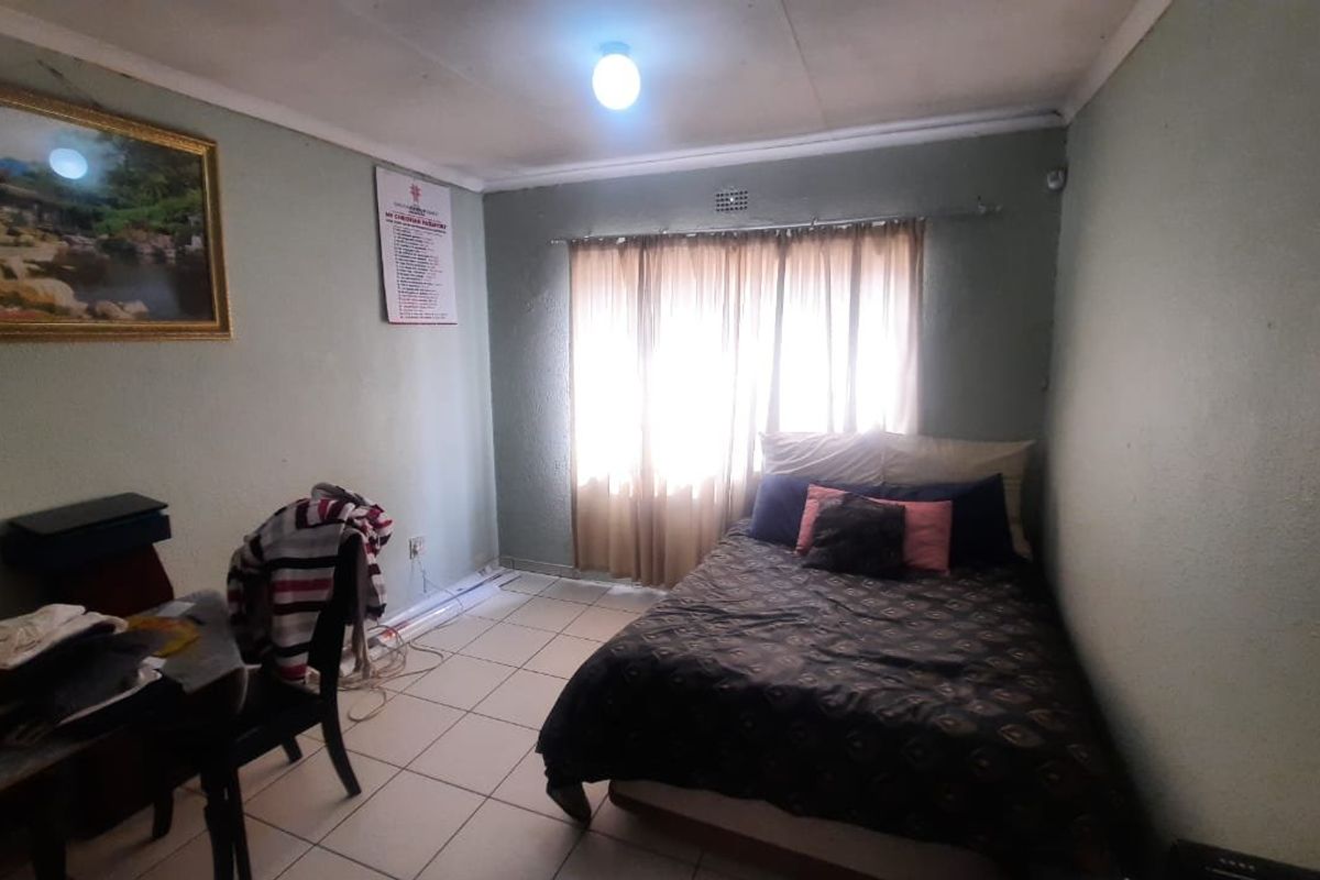 A bedroom featuring tiled flooring and a window with curtain rods, requiring cosmetic updates to improve the overall finish and condition.
