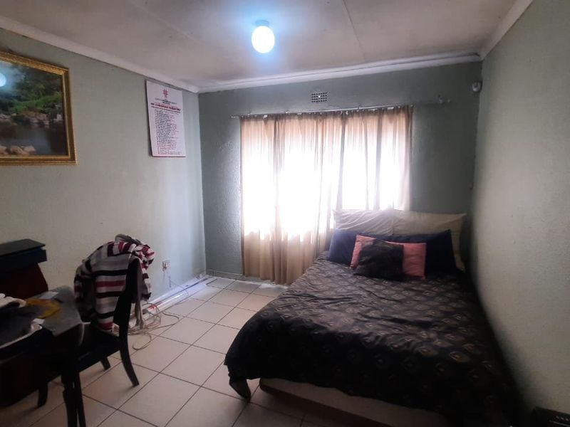 A bedroom featuring tiled flooring and a window with curtain rods, requiring cosmetic updates to improve the overall finish and condition.