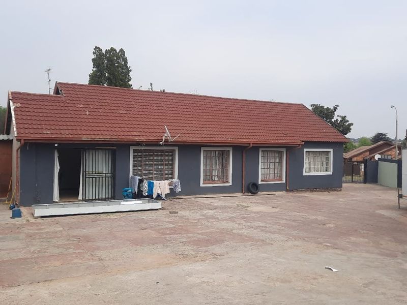 Rear view of the townhouse featuring a tiled roof, paved courtyard area, and security features on windows and doors.