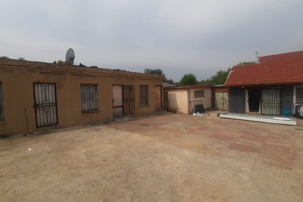 Rear exterior view of the townhouse property featuring a paved courtyard area and multiple access points with security gates and bars.