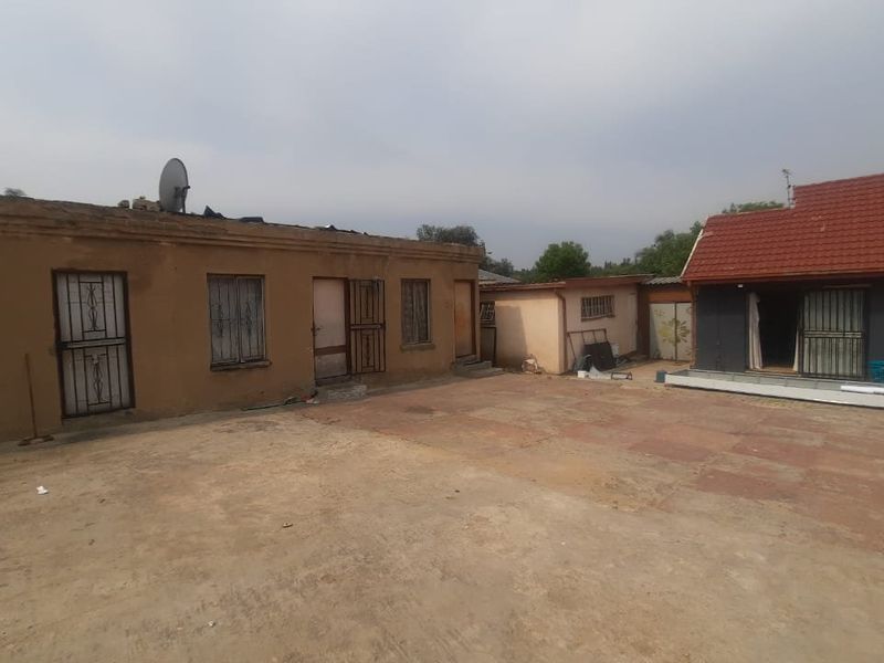 Rear exterior view of the townhouse property featuring a paved courtyard area and multiple access points with security gates and bars.