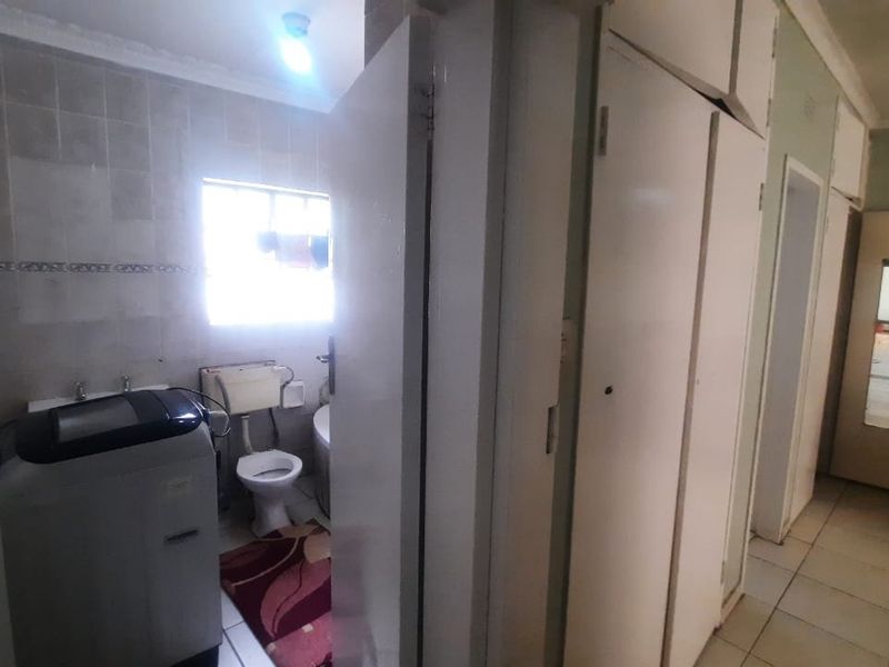 A dated bathroom featuring tiled walls, a bathtub, and a toilet, adjacent to a hallway with built-in storage cupboards.