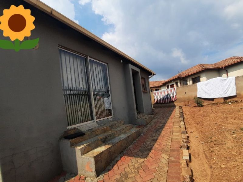 Rear exterior view of the house featuring a paved walkway, tiled steps leading to a sliding glass door, and a surrounding perimeter wall.