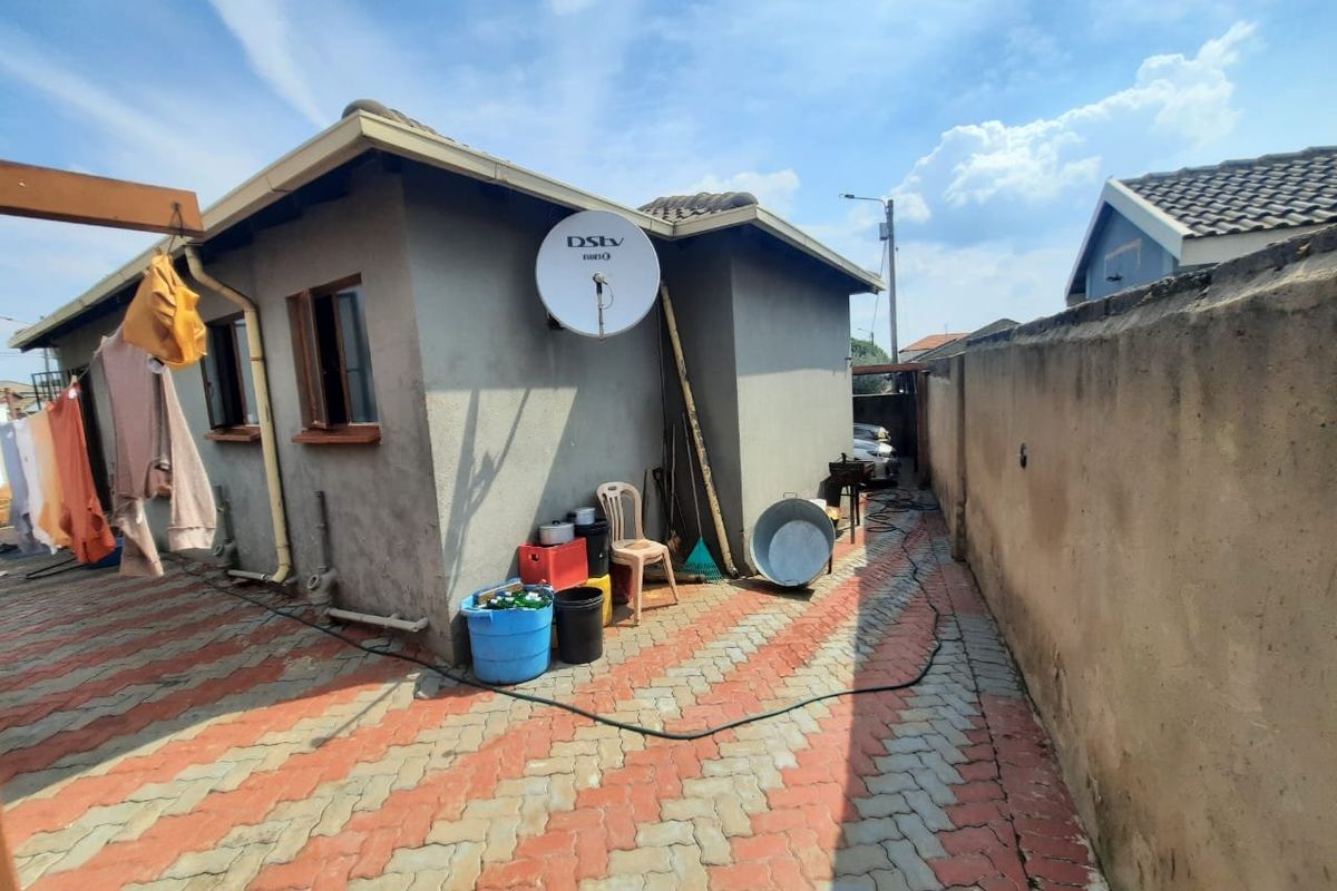 Rear exterior view of the property featuring a paved courtyard area, boundary wall, and satellite dish installation.