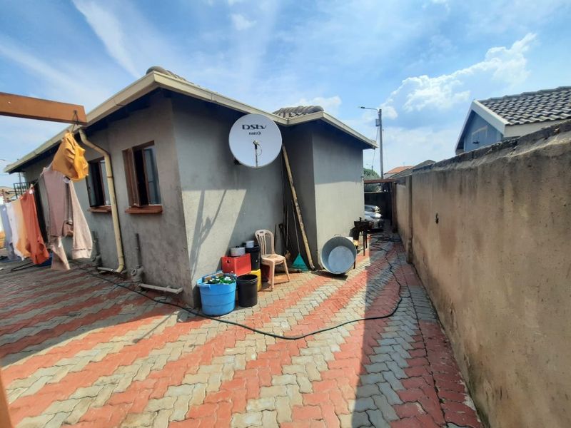 Rear exterior view of the property featuring a paved courtyard area, boundary wall, and satellite dish installation.