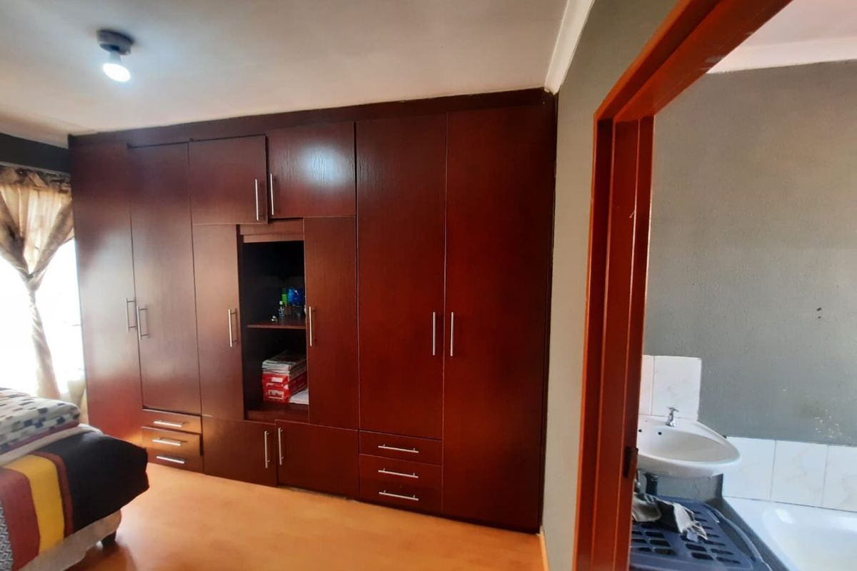 Bedroom featuring extensive dark wood built-in cupboards and laminate flooring, with an adjacent view into a bathroom area.