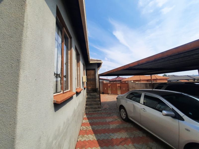 Side exterior view of the property featuring a paved driveway, a covered carport, and a secure entrance door.