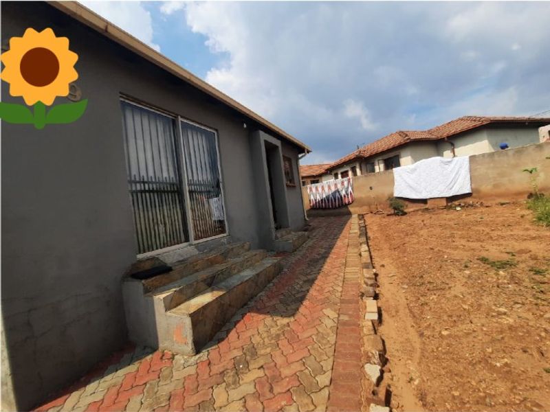 Rear exterior view of the property featuring a paved walkway, concrete steps leading to a sliding glass door, and an unfinished garden area.