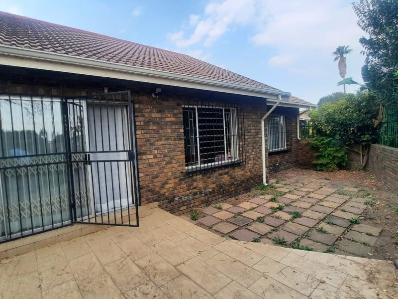 Rear exterior view of the townhouse featuring a brick facade, tiled roof, security-fitted windows and doors, and a paved patio area with garden space.