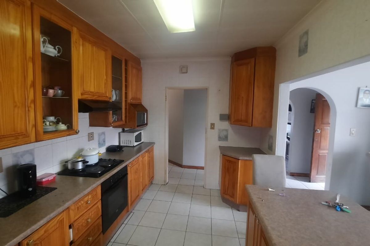A functional kitchen featuring traditional wooden cabinetry, laminate countertops, built-in oven, and hob, with tiled flooring and direct access to adjacent living areas.
