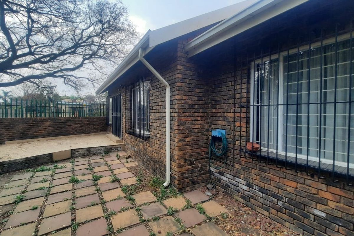 Rear exterior view of the townhouse featuring a face brick facade, security bars on windows, and a paved patio area with boundary walling.